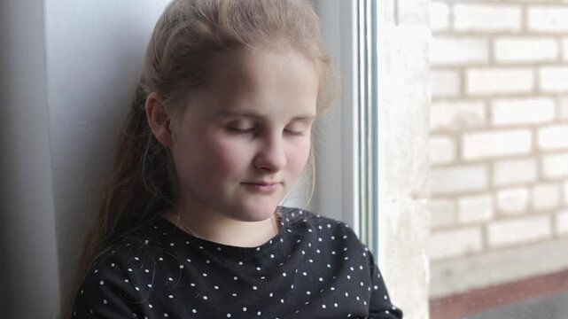 Teenage girl reading a book sitting on a windowsill and reasoning. Preparing homework. Reading a book and discussing it. Portrait of a smart, well-read girl sharing her thoughts