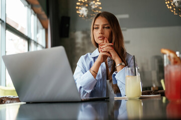 Cocktail is on the table. Beautiful woman with laptop is in the bar