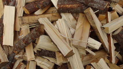  a pile of chopped firewood. The pieces are irregular in shape and size, with some having bark on them. The wood is mostly light brown, with some darker brown areas where the bark is present