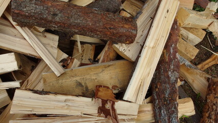 a pile of chopped firewood. The pieces of wood vary in size and shape, with some having bark still attached. The wood appears to be freshly cut, as indicated by the light color