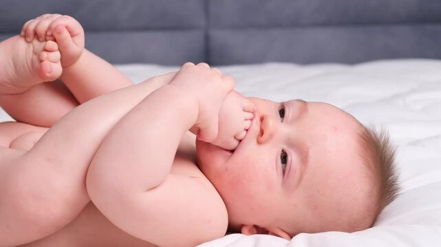 infant young little baby boy children trying to eat chew his legs. Lies on his back put into mouth foot finger toes teether teeth pain tooth breaks through the gum