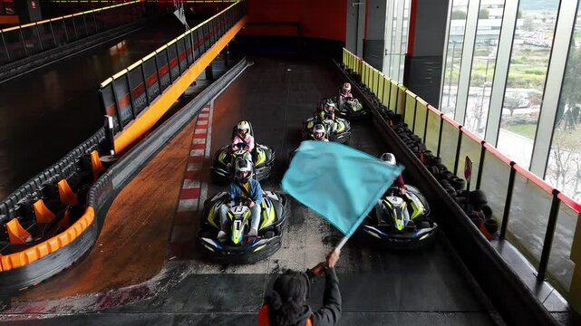group of go-kart drivers crossing the finish line, with an official waving the checkered flag. Go-Kart Racers Crossing Finish Line as Checkered Flag Waves