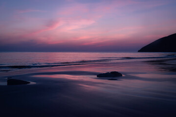 Tranquil twilight on serene beach, soft pink and purple hues reflecting calm ocean waters with reflections, silhouettes of rocks, peaceful beauty coastal landscape dusk, Mawgan Porth, Cornwall, UK