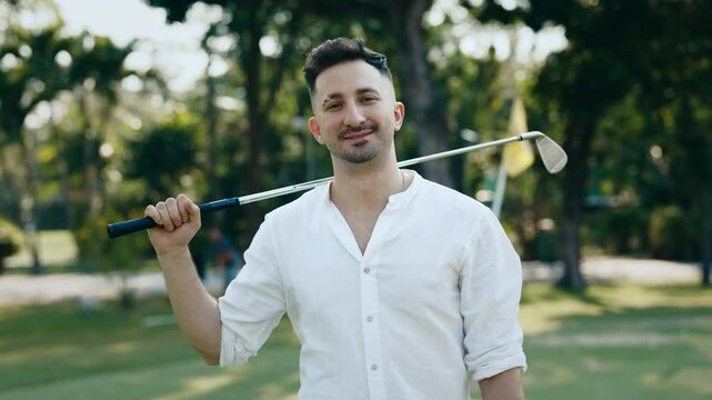 Happy bearded man with driver on shoulder smiling to camera in shady park portrait. Successful golf player enjoys training in luxury sports club. Positive sportsman at competition