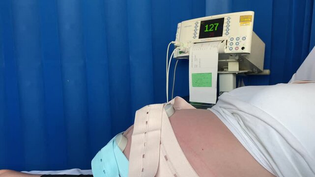 A pregnant women lays on a hospital bed her babies heartbeat being monitored on a cardiotocograph machine 