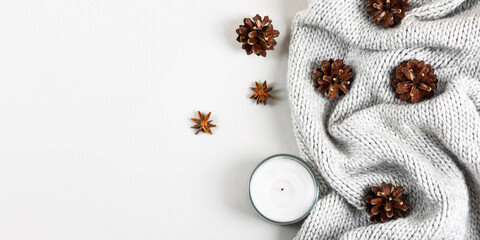 Cozy winter gray background made of knitted blanket, white candle, cones and star anise with place for text and greetings. Concept of warm and cozy home atmosphere