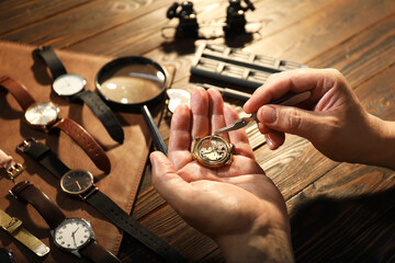 Man fixing mechanism of vintage wrist watch at wooden table, closeup