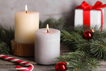 Burning candles, Christmas decor and fir tree branches on wooden table, closeup