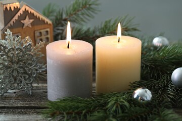 Burning candles, baubles and fir tree branches on wooden table, closeup