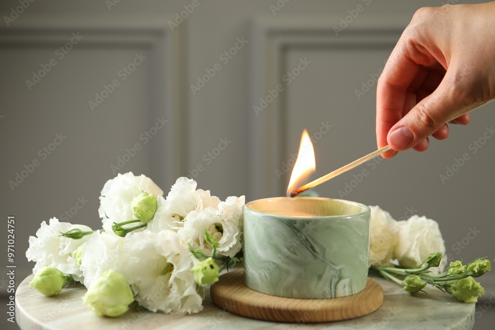 Poster Woman lighting candle at table with beautiful flowers, closeup