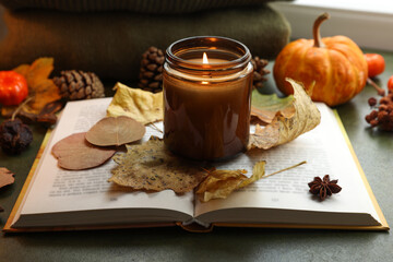 Burning candle, autumn decor and open book on green background