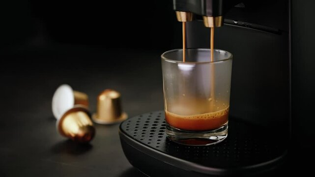 Espresso coffee machine brewing fresh coffee into a clear glass with coffee pods in the background.