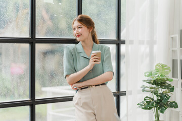 Contemplative Coffee Break: Young woman in stylish office attire enjoys a moment of reflection by the window, coffee in hand, embodying modern work-life balance.