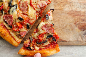 A man's hand takes a cut slice of pizza from a wooden board. High quality photo