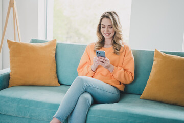 Obraz premium Photo portrait of attractive young woman sit couch hold gadget dressed orange outfit cozy day light home interior living room
