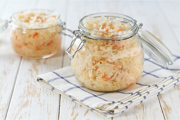 glass storage jar with sauerkraut and carrots on white kitchen table.