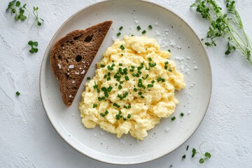 A plate of scrambled eggs garnished with chives and a slice of dark bread.