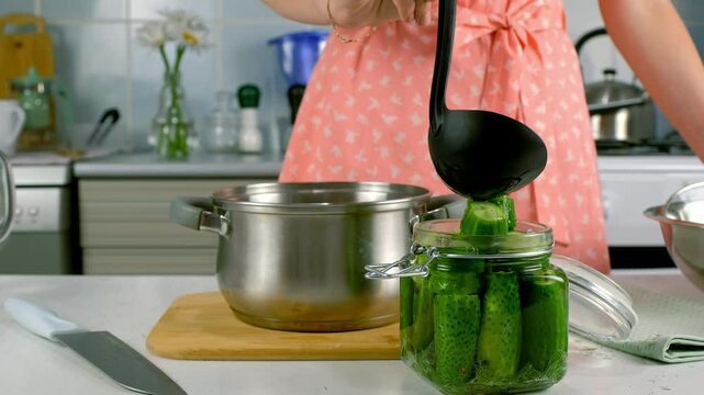Woman pouring saline to cucumbers in glass jar to cook pickles on kitchen at home, hands close-up. Cuisine, culinary, prepare cook dish, domestic food, recipe, fresh organic ingredients concept.