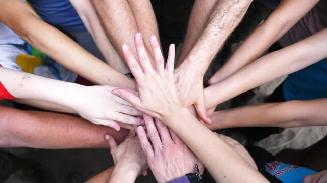 Male and female hands stacking together one by one in unity outdoor. Group of unrecognizable best friends putting their arms in centre of circle and raising them up. Friendship and teamwork. Top view