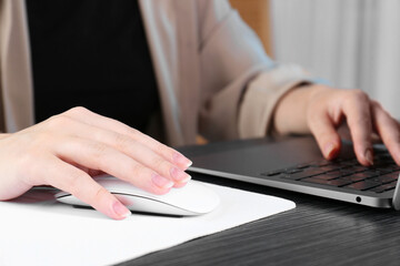 Fototapeta premium Woman using computer mouse while working with laptop at black wooden table, closeup