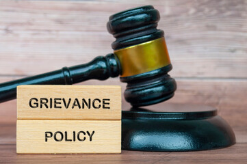 Grievance policy text engraved on wooden blocks with gavel background. Grievance policy concept