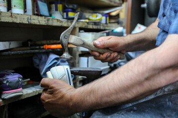 Diligent cobbler is working on shoe sole using hammer at his dark workplace.