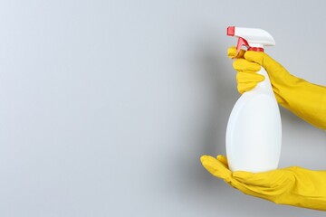 Woman holding toilet cleaner in spray bottle on light background, closeup. Space for text