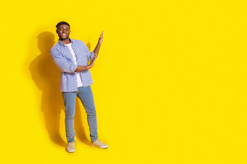 Full length photo of cheerful positive guy dressed checkered shirt pushing arms emtpy space isolated yellow color background