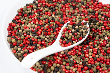 Different varieties of peppercorns, red, green, black and white peppers in a spoon