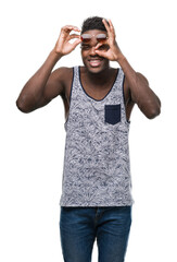 Fototapeta premium Young african american man wearing sunglasses with happy face smiling doing ok sign with hand on eye looking through fingers