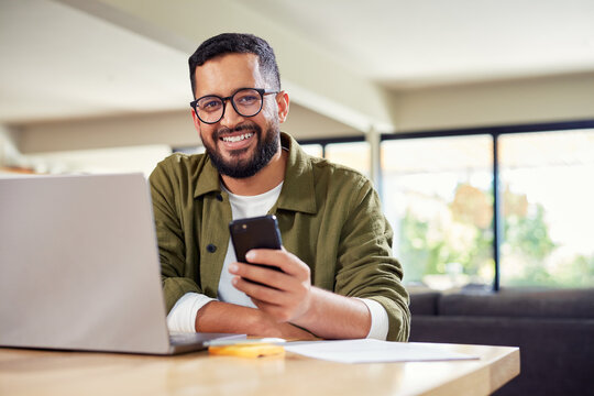 Smiling man using laptop and phone at home
