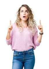 Beautiful young blonde woman over isolated background amazed and surprised looking up and pointing with fingers and raised arms.