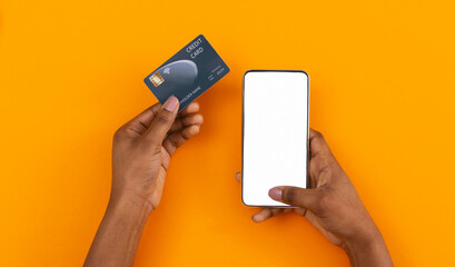 Online payment. Smartphone with blank screen and credit card in black female hands on orange background, copy space