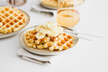 Belgian waffles with banana and condensed milk on white table