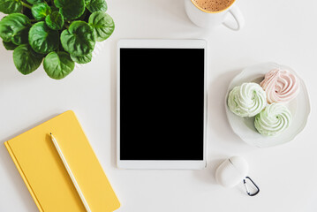 Mock-up digital tablet with empty screen, notebook, coffee cup, food and plant on white table. Top view. Flat lay