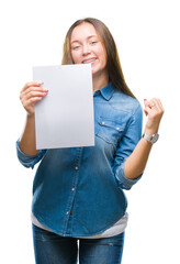 Young caucasian woman holding blank paper sheet over isolated background screaming proud and celebrating victory and success very excited, cheering emotion