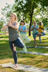 Blond woman in activewear keeping left feet on upper part of right leg while showing new yoga exercise to elderly people