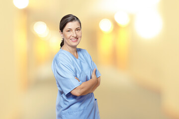 Friendly smiling mature nurse in a blue scrub, against a blurred light yellow interior background,...