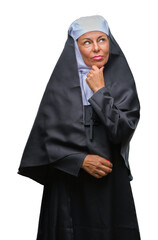 Middle age senior christian catholic nun woman over isolated background looking confident at the camera with smile with crossed arms and hand raised on chin. Thinking positive.