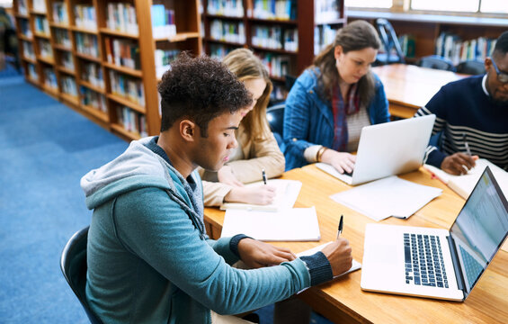Students, group and learning with notes, laptop and development in campus library at university. People, men and women with books, solution and reading by computer with planning for exam at college