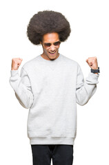 Young african american man with afro hair wearing sunglasses very happy and excited doing winner gesture with arms raised, smiling and screaming for success. Celebration concept.