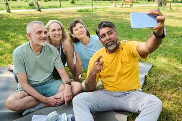 Confident multiethnic mature man pointing at screen of smartphone while taking selfie or recording...