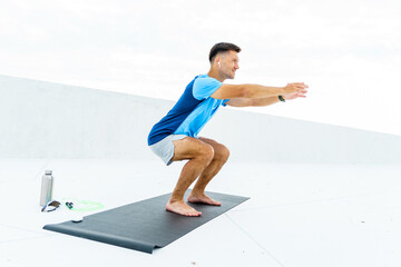 A man performs squats on a mat outdoors, focusing on balance and form, with fitness accessories...
