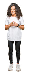 Fototapeta premium Young beautiful woman with curly hair wearing white t-shirt Hands together and fingers crossed smiling relaxed and cheerful. Success and optimistic