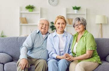 Fototapeta premium Portrait of a happy family featuring an adult daughter embracing elderly parents on the couch at home living room. Love, togetherness and strong family bond, radiating joy and affection.