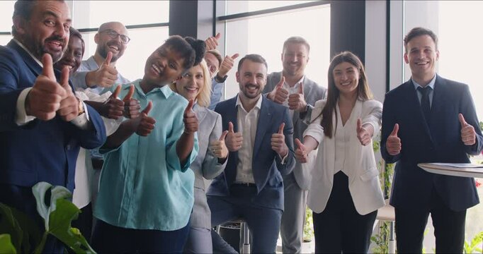 Smiling diverse coworkers showing thumbs up, looking at camera. Happy male and female company employees team or group of staff standing and celebrating success. Teamwork, job satisfaction concept.