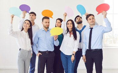 Team of business people with speech bubbles in their hands. Group of happy male and female corporate employees standing on a white office background holding up colorful mock up paper cards