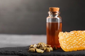 Honey tincture, honeycomb and pile of propolis granules on table, closeup. Space for text