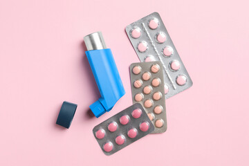 Asthma inhaler and pills on pink background, flat lay