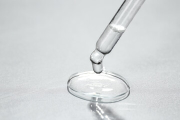 Cosmetic oil dripping from pipette on light grey background, closeup